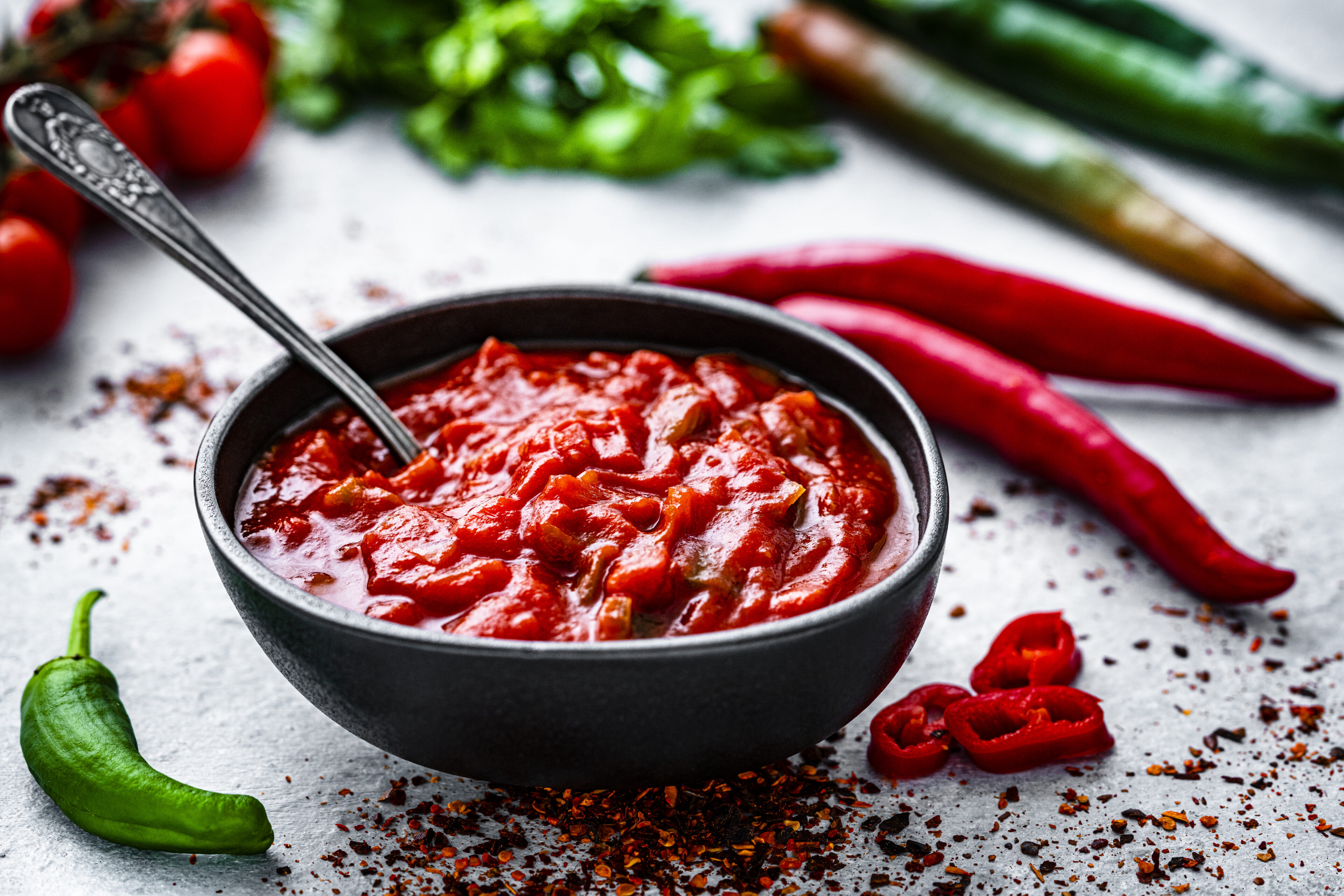 Red hot chili sauce with ingredients shot on gray table. High resolution 42Mp studio digital capture taken with Sony A7rII and Sony FE 90mm f2.8 macro G OSS lens