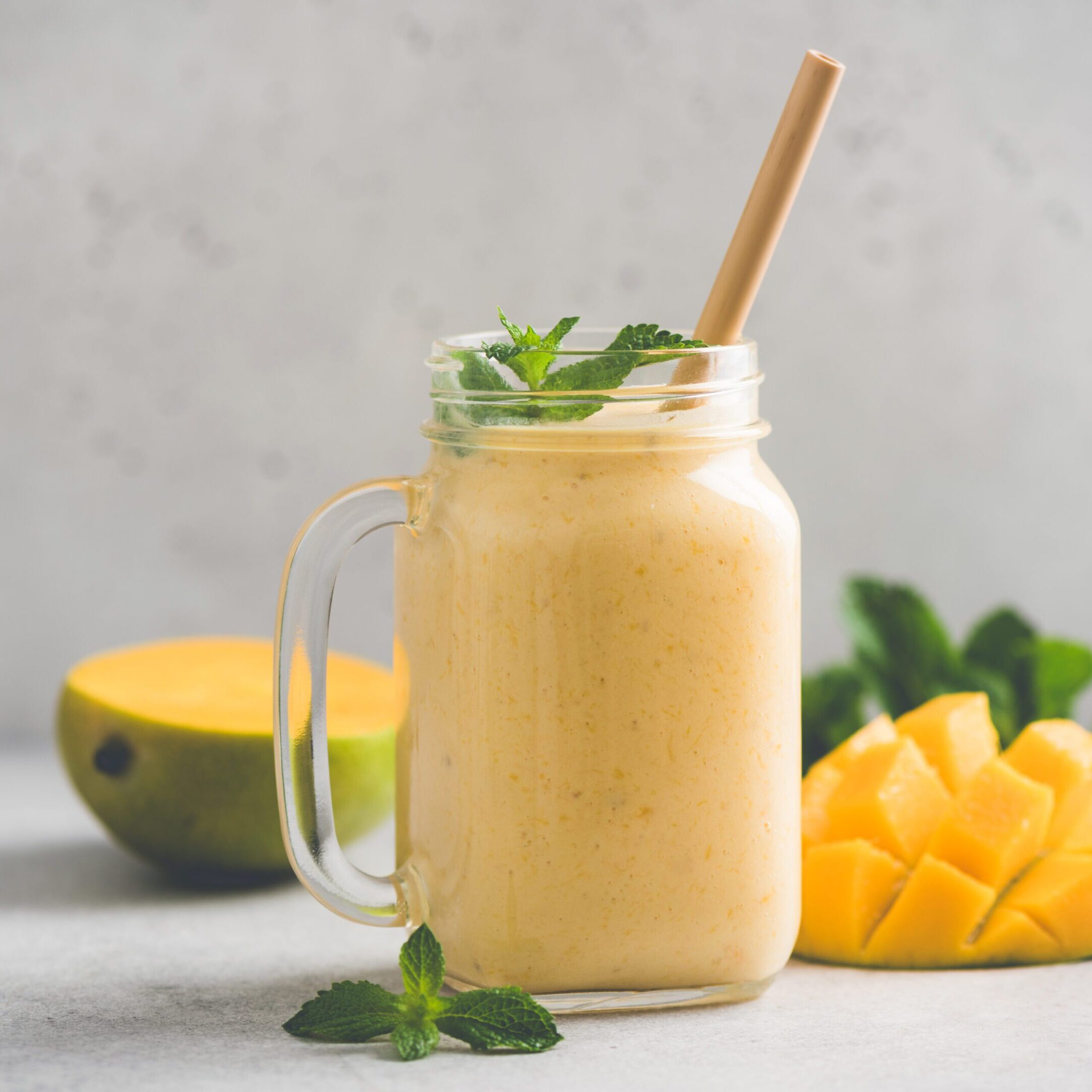 Delicious mango smoothie in glass jar on grey background with copy space. Refreshing summer drink